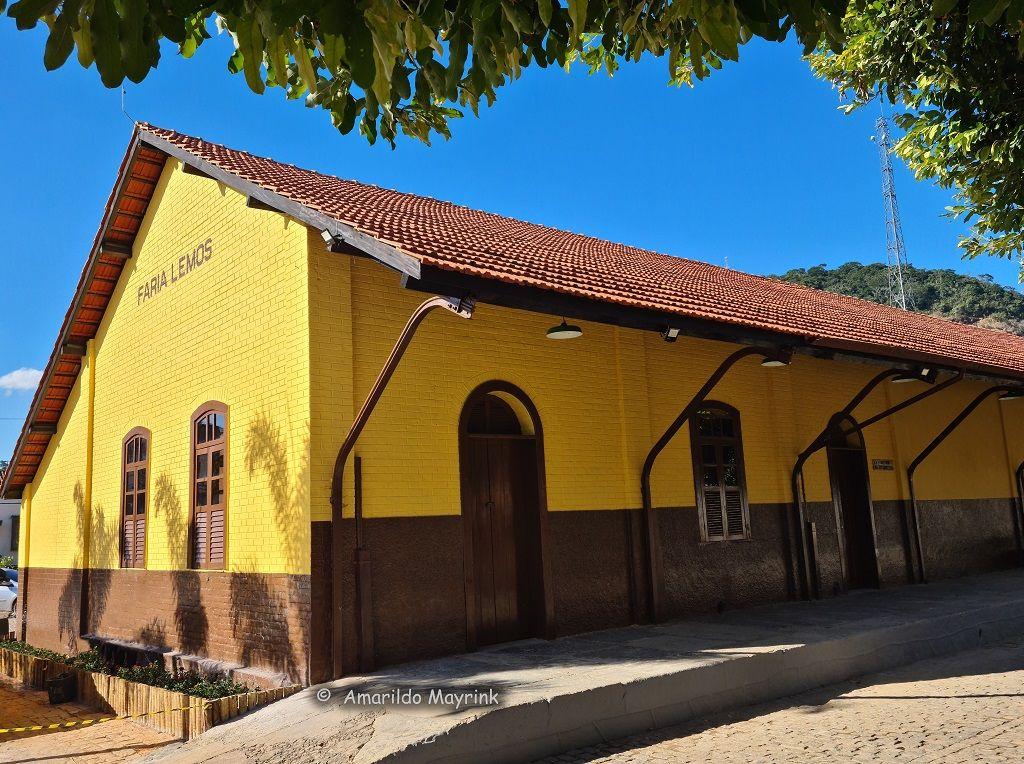 Yellow and brown building with red tiled roof and arched windows, surrounded by trees.